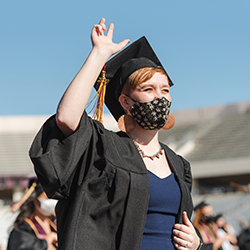 a masked graduate raises her hand doing the txst hand sign