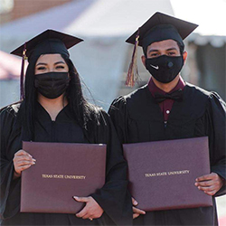 two masked students holding texas state diploma covers